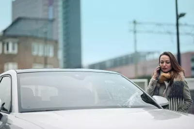 A person at the phone next to a car with a damaged windshield
